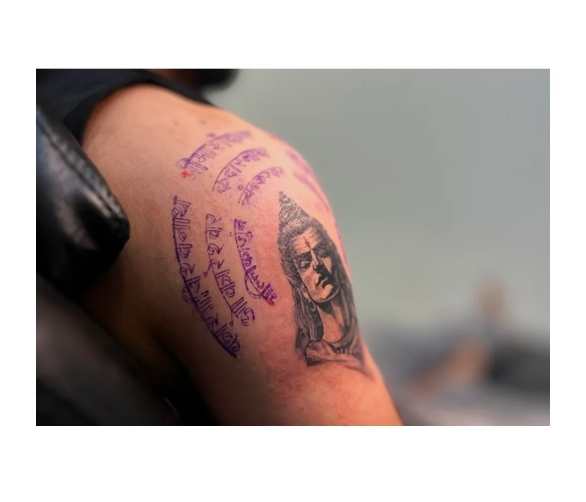 Shiva portrait and Sanskrit script tattoo across an upper arm